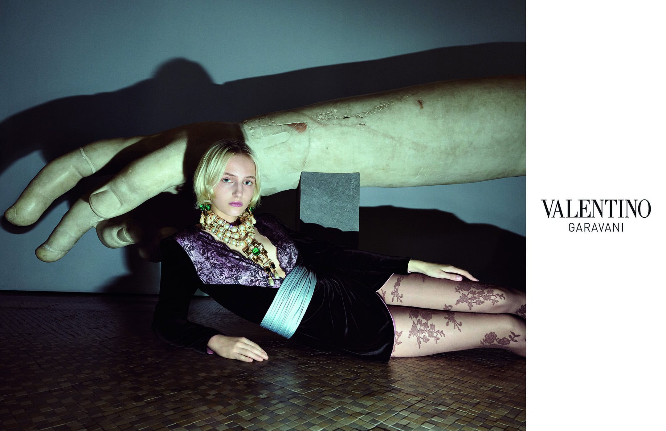 Model Apolline Rocco Fohrer reclining in a black velvet dress and floral tights beneath a giant sculpted hand for Valentino.