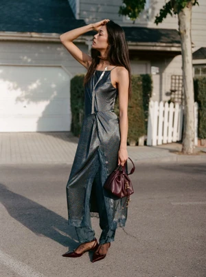 Model Jade Nguyen poses on a residential street wearing a shimmering grey slip dress over matching pants with a burgundy handbag.