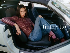Model Jade Nguyen reclines in the front seat of a white convertible car wearing a burgundy knit top and blue jeans.