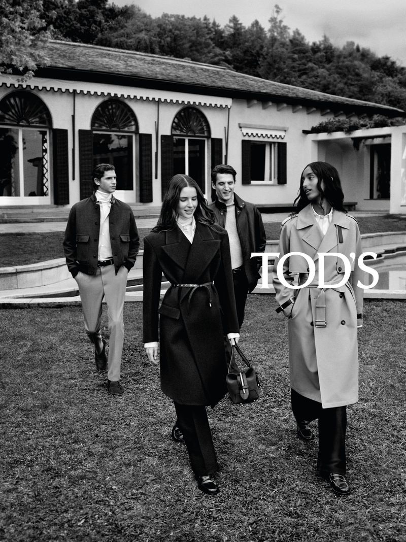 Four models walking across a lawn outside a villa wearing tailored coats and jackets in black and white for Tod's.