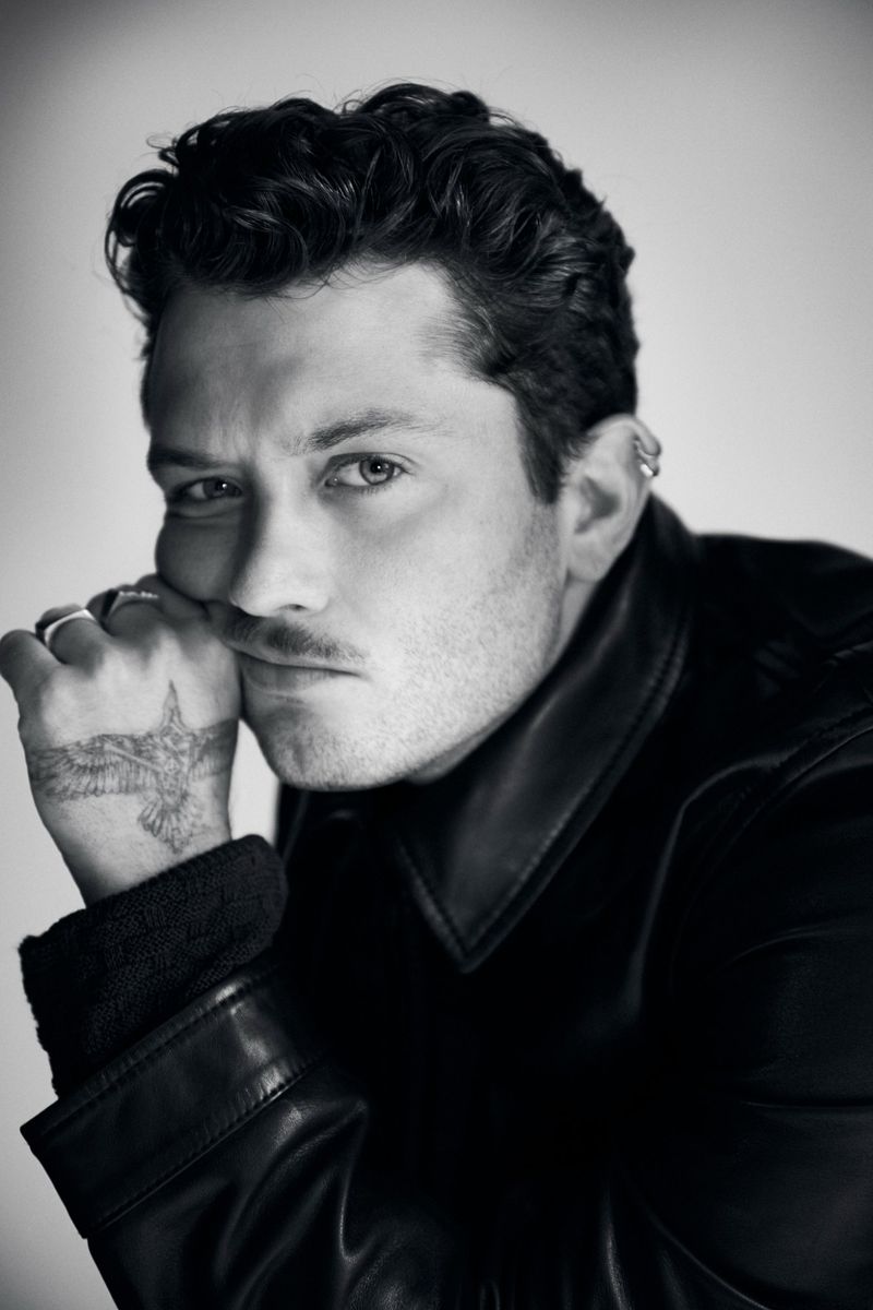 Black and white close-up portrait of Raff Law resting his chin on a tattooed hand wearing a dark leather jacket.