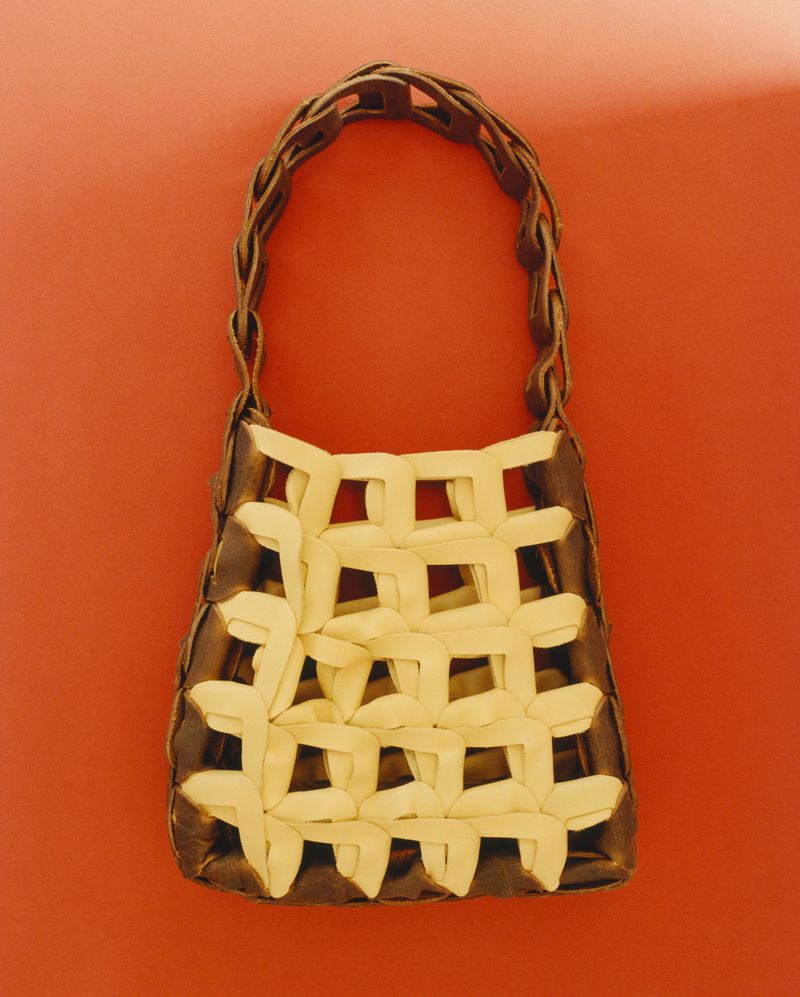 Interlocking cream and dark brown woven leather shoulder bag with a linked strap against a warm orange background.