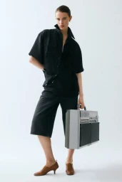 Model wearing a black short-sleeve shirt and knee-length shorts holding a grey vintage boombox against a white background.