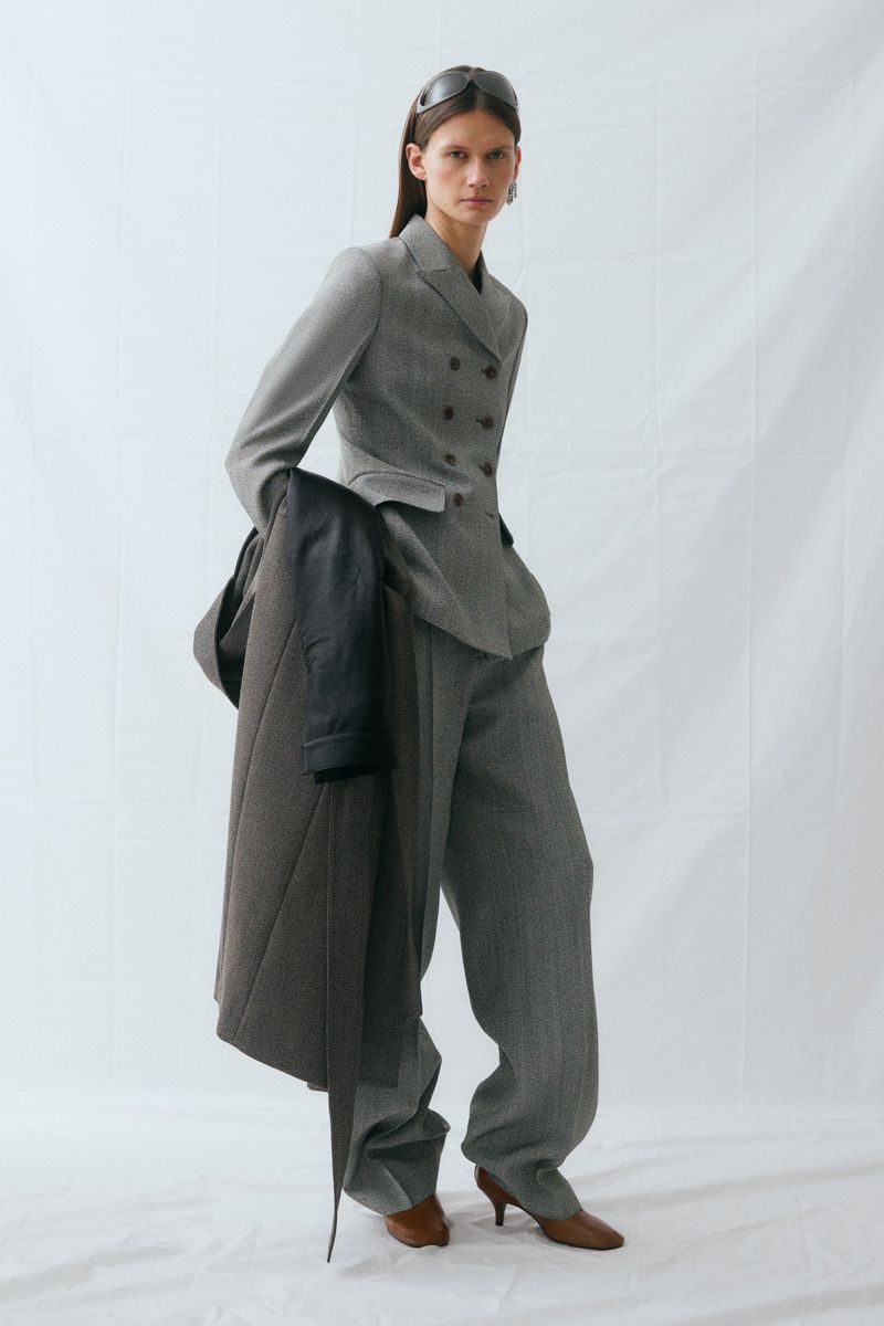 Model posing in a tailored grey double-breasted suit and brown kitten heels against a white backdrop.