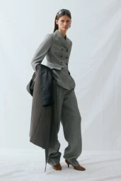 Model posing in a tailored grey double-breasted suit and brown kitten heels against a white backdrop.