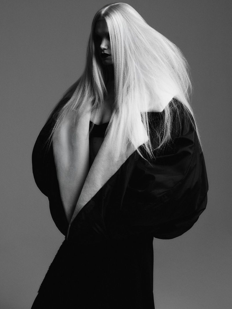 Monochrome fashion portrait of model Sasha Dom with long voluminous hair in a sculptural black puff sleeve coat for Telva.