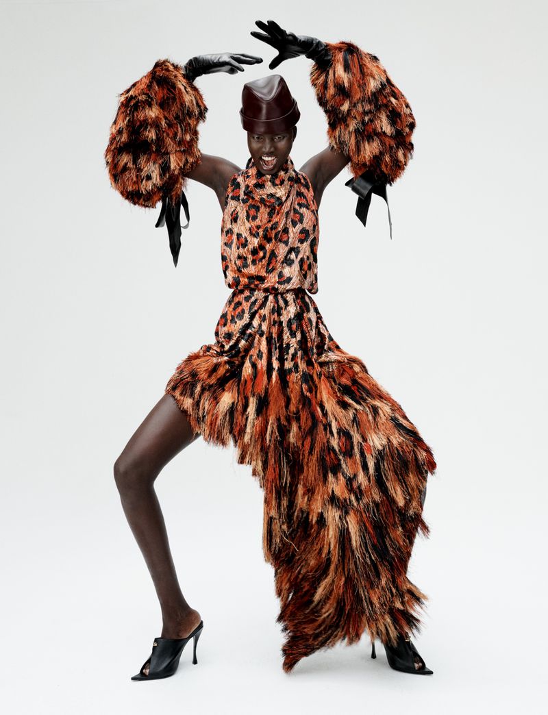 Model Aluel Keror posing dynamically in a feathered leopard print dress with oversized sleeves against a white studio background.