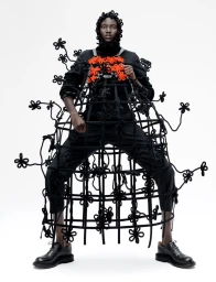 Model Aluel Keror wearing an avant-garde black floral cage structure over black apparel against a white studio background.