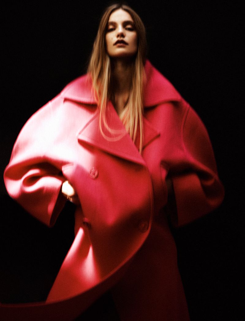 Model Taylor D posing in an oversized bright pink structured coat against a solid black background.