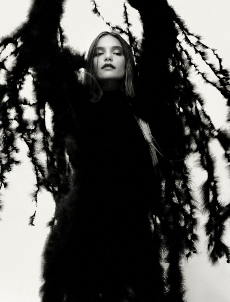 Model wearing an elaborate textured black feathered coat with wing-like silhouettes against a bright white background.