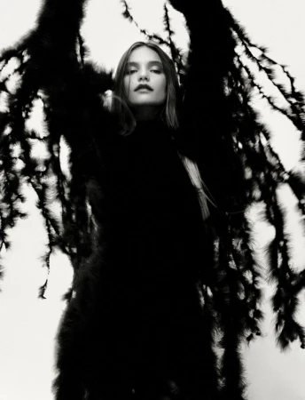 Model wearing an elaborate textured black feathered coat with wing-like silhouettes against a bright white background.