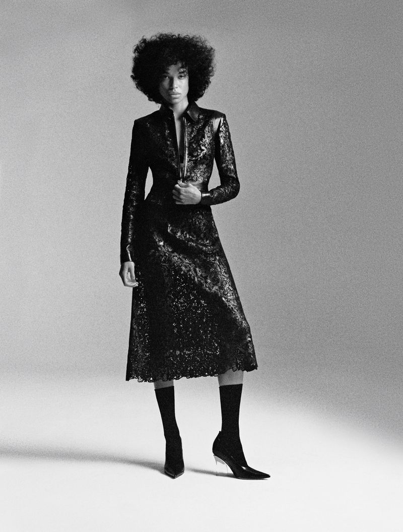 Model Lara Menezes poses in a black sequined midi dress with black ankle socks and pointed heels against a studio background.