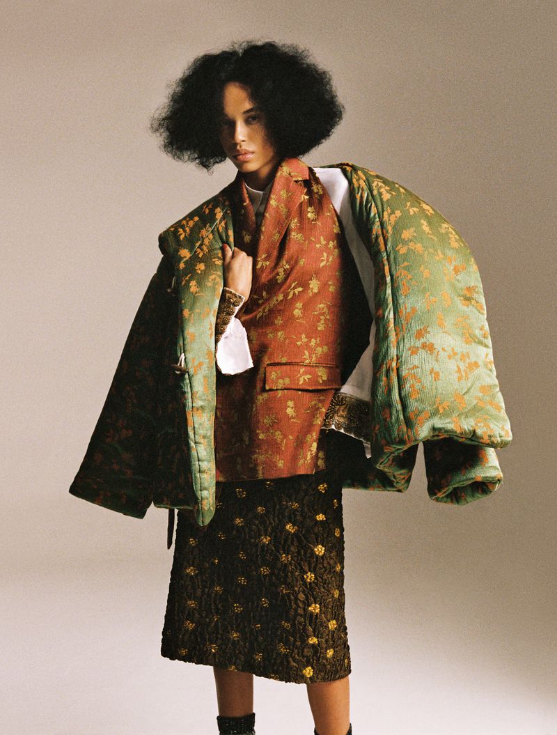 Model Lara Menezes wearing an oversized green quilted floral jacket and rust brocade blazer against a neutral studio background.
