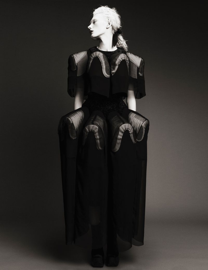 Model Ivy Stewart poses in an avant-garde sculptural black Comme des Garcons dress against a dark studio backdrop.