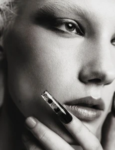 Monochrome close-up portrait of model Ivy Stewart with dark eye makeup touching her face with a sculptural black-tipped nail.