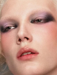 Extreme close-up beauty portrait of model Ivy Stewart with smoky purple eye makeup and bleached eyebrows looking toward the camera.