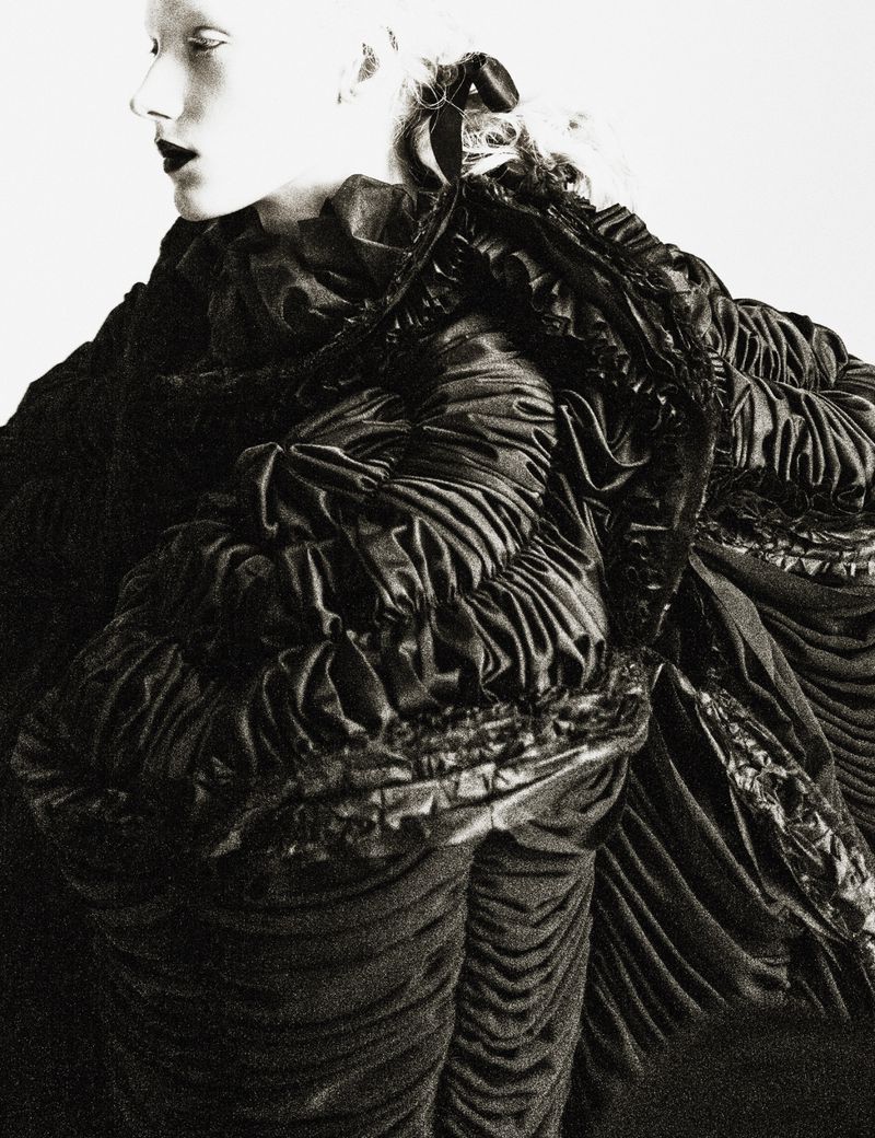 Model Ivy Stewart in profile wearing an voluminous ruched black Comme des Garcons garment against a stark white background.