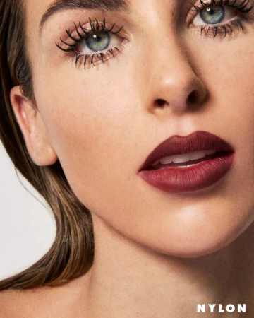 Close-up beauty portrait of a woman with bold matte burgundy lipstick and dramatic spidery eyelashes against a light background.