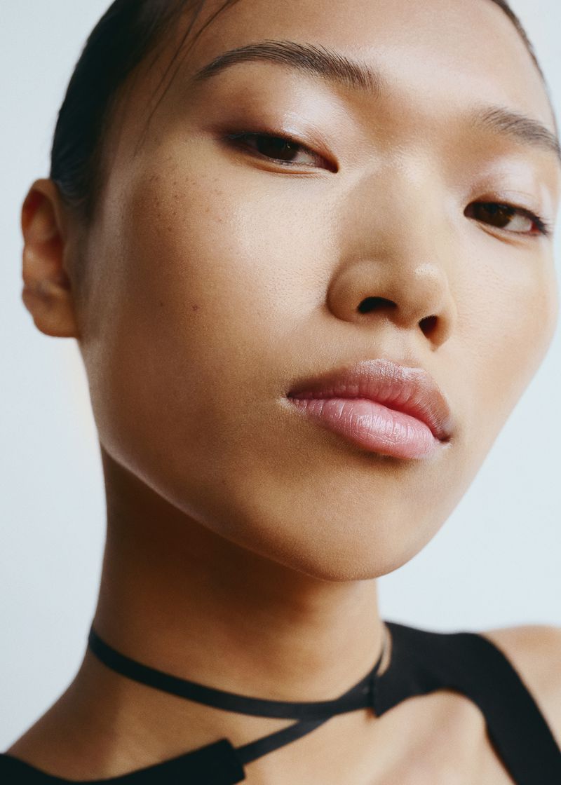 Close-up beauty portrait of an East Asian woman with natural makeup, looking at the camera against a neutral studio backdrop.