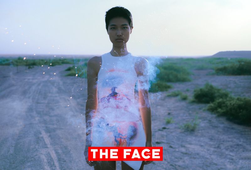 East Asian model in a sleeveless white dress standing on an arid dirt path at dusk with smoke effects and The Face China logo.