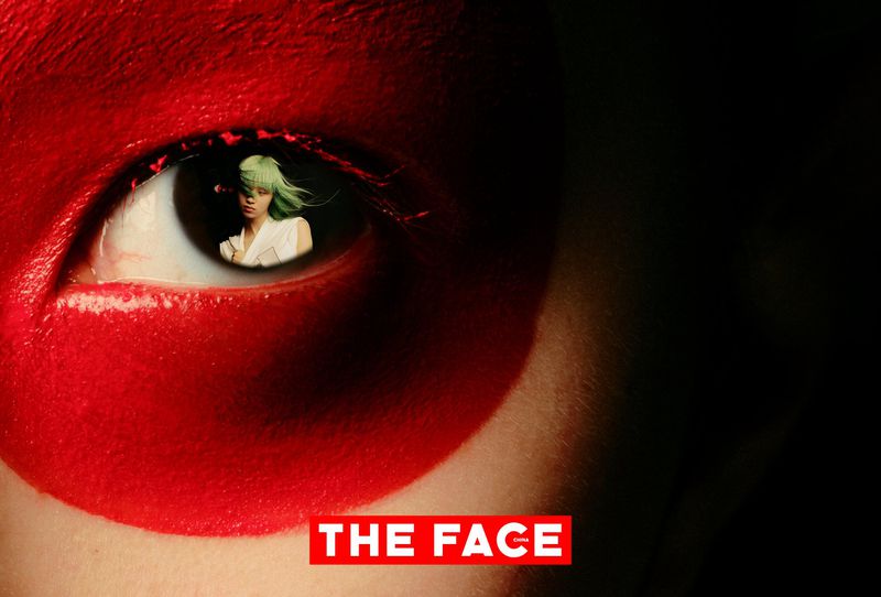 Extreme close-up of an eye framed in circular red paint with a reflection of a model with green hair in the iris.