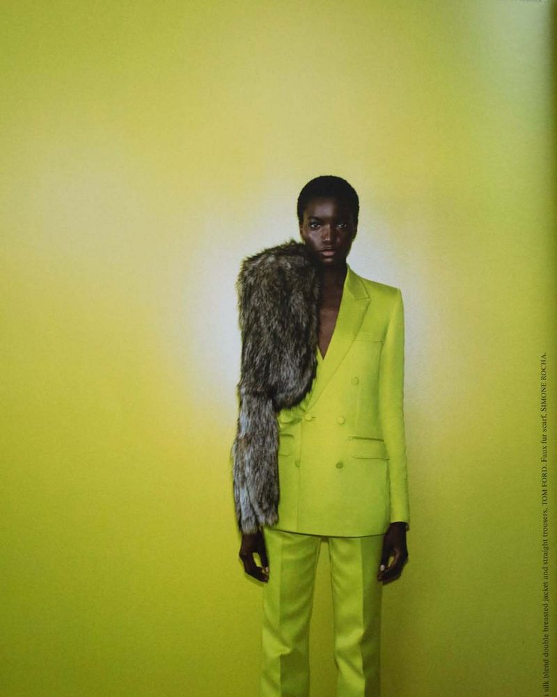 A slender African American woman in a bright lime green suit stands against a matching backdrop, accentuated with a large fur stole.
