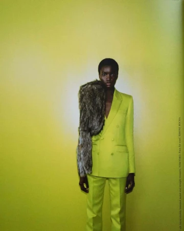 A slender African American woman in a bright lime green suit stands against a matching backdrop, accentuated with a large fur stole.