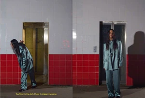 Model wearing a blue satin suit standing in front of elevator doors with red and white tiled walls.