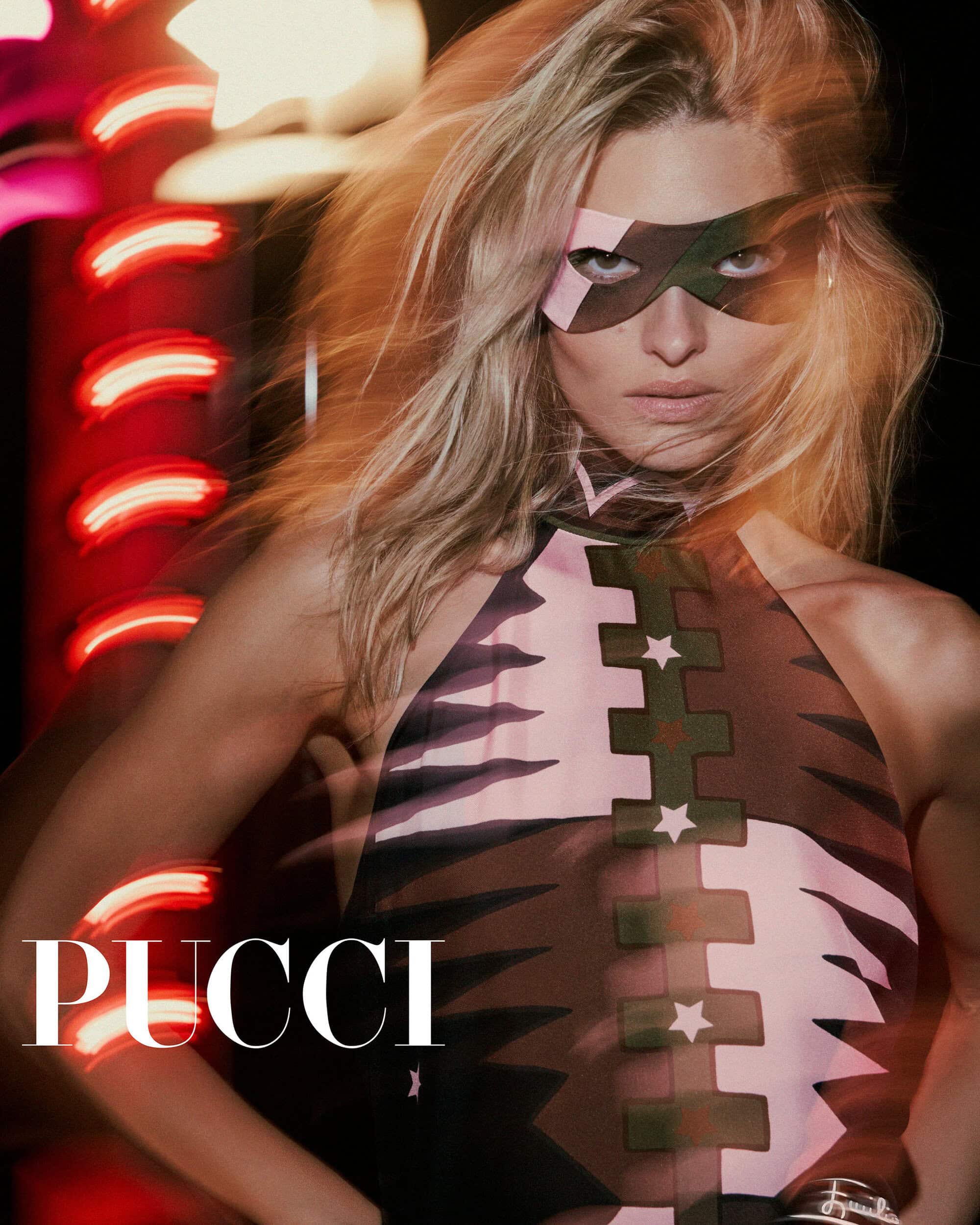 Model Grace Elizabeth wears a geometric eye mask and graphic halter dress beside glowing red neon lights for Pucci.