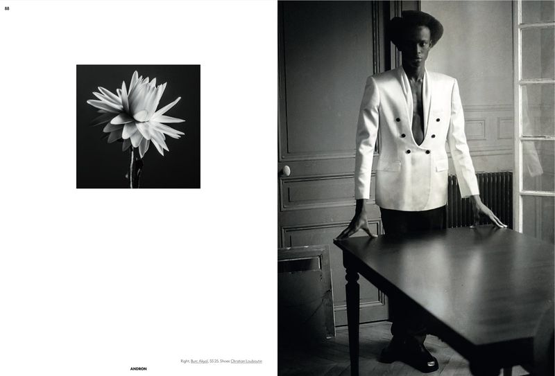 Monochrome fashion shot of a Black male model in a white jacket at a table, alongside a flower image on a magazine spread.