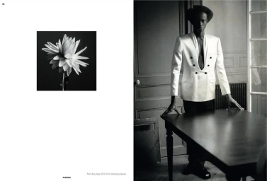 Black and white editorial layout with a flower close-up on the left and a man in a white blazer leaning over a wooden table on the right.
