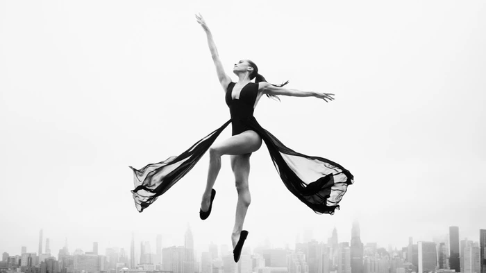 Misty Copeland leaping mid-air in a black leotard against a cityscape background for Stuart Weitzman Fall 2026