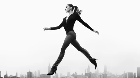 Misty Copeland leaping in black bodysuit and high boots against a city skyline for Stuart Weitzman