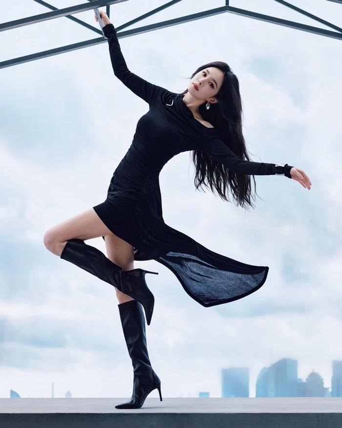 Yang Mi in a black dress and boots striking a dance pose on a rooftop for Stuart Weitzman Fall 2026