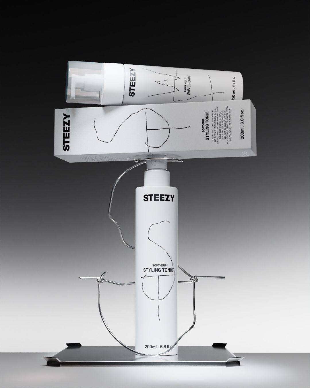 STEEZY haircare bottles and packaging box stacked on a bent wire stand against a grey gradient backdrop.