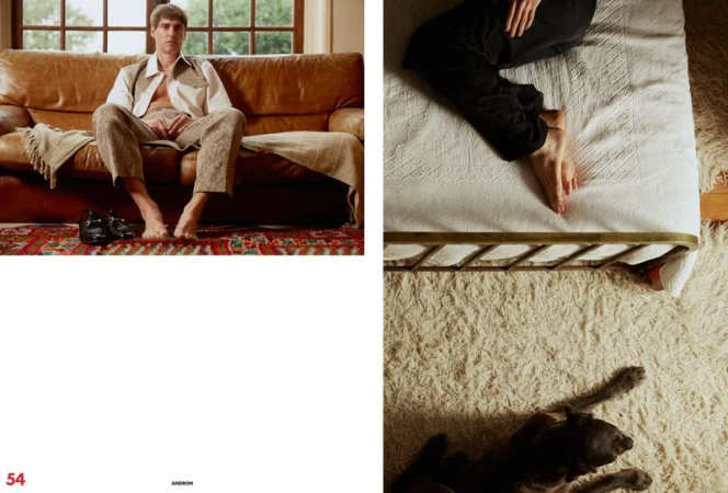 A man in patterned pants and shirt poses barefoot on a leather sofa, with a dog lying on a white rug on the right.