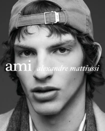 Black and white close-up portrait of a man wearing a backwards baseball cap with an Ami Alexandre Mattiussi logo overlay.