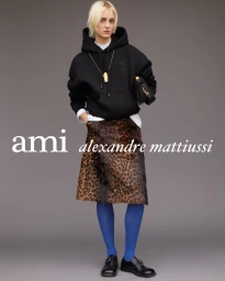 Model posing in a black oversized hoodie, leopard print skirt, and cobalt blue tights against a grey studio backdrop.