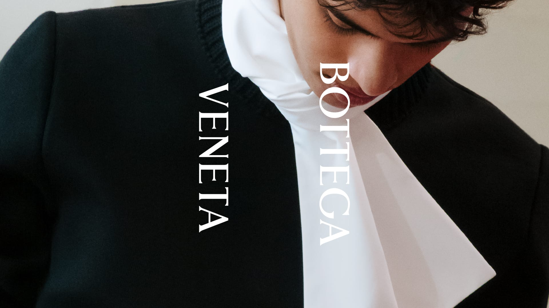 Close-up of a model wearing a black sweater with a crisp white scarf draped over the collar and the Bottega Veneta logo overlaid.