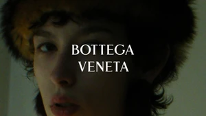 Close-up portrait of a model wearing a textured fur hat overlaid with white Bottega Veneta typography across the center frame.