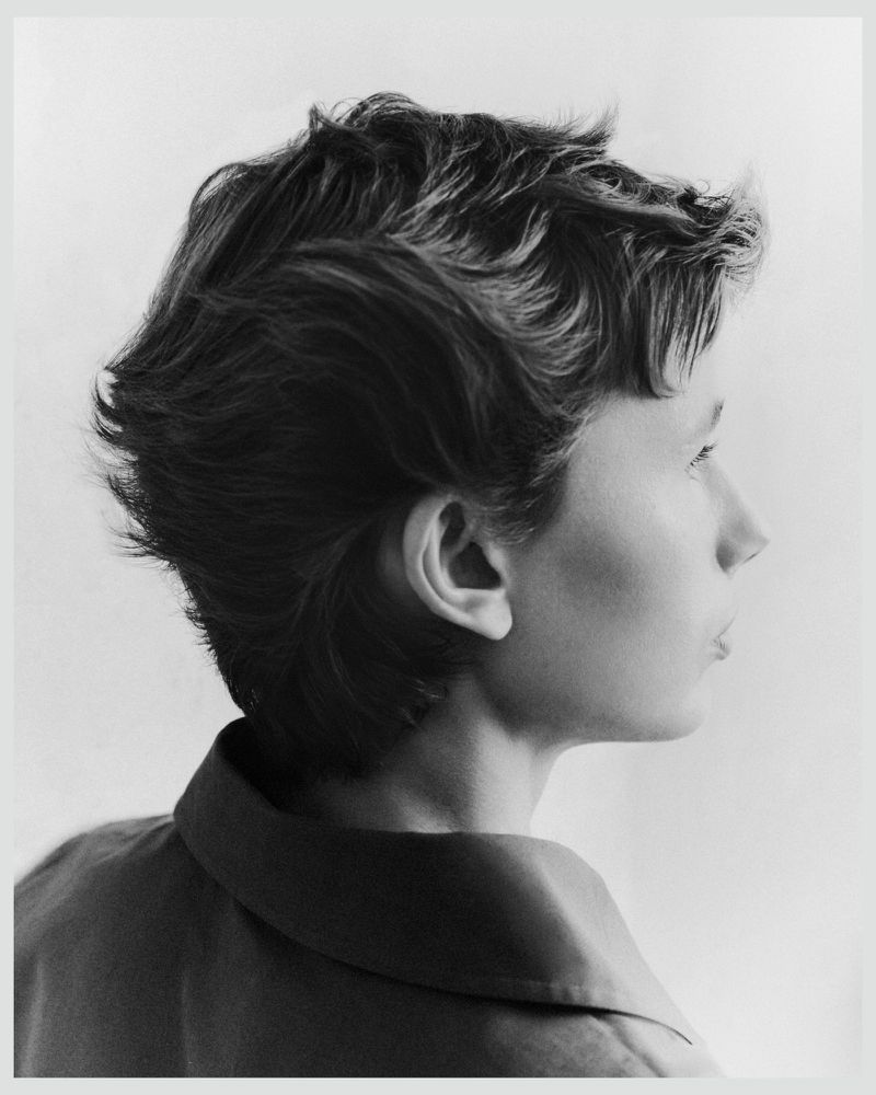 Black and white profile portrait of model Nora Svenson with short textured hair wearing a collared shirt against a light background.
