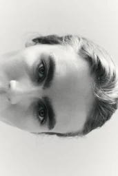 Black and white close up portrait of a woman's eyes, defined eyebrows, and forehead against a plain pale background.