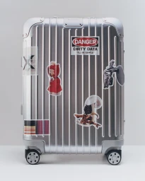 Silver grooved RIMOWA aluminum suitcase decorated with graphic stickers against a plain white studio backdrop.
