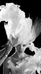 Anya Taylor-Joy wears an oversized white sculptural ruffled headpiece and matching garment against a stark black background.