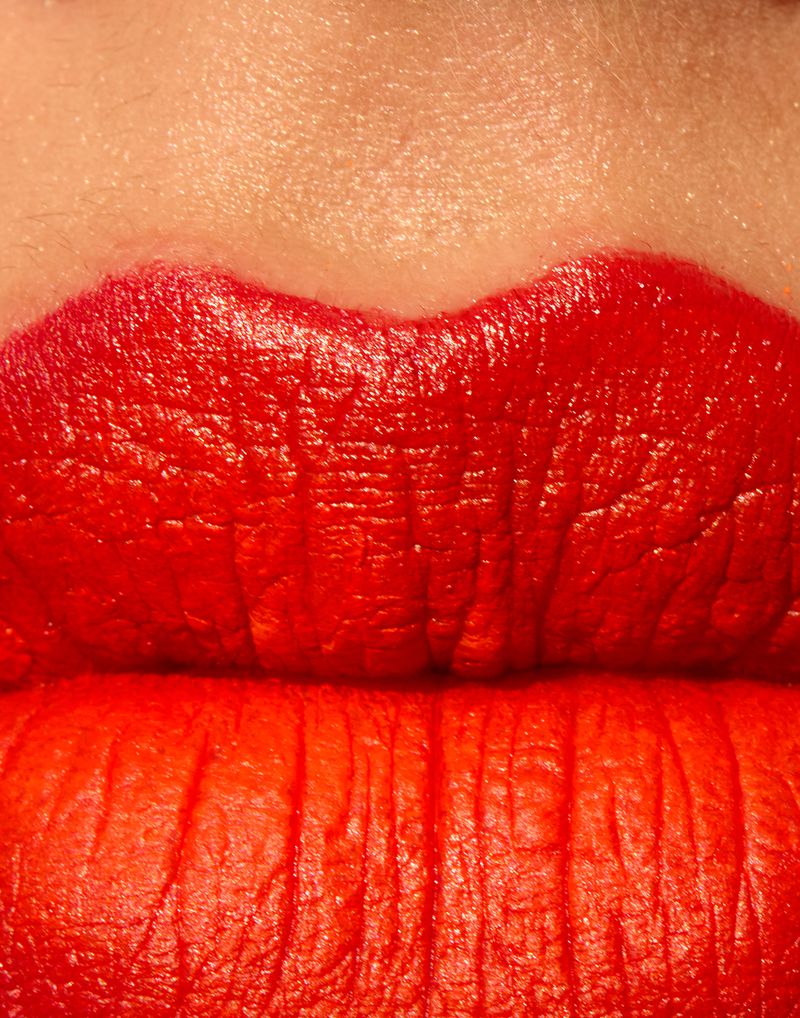 Macro close-up of lips painted with vibrant matte red lipstick, highlighting skin and lip texture.