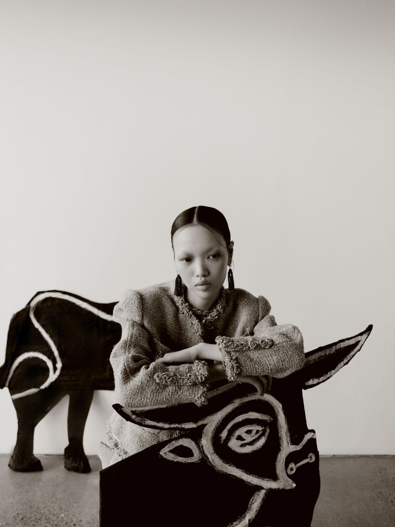 Model Weiyi Fang wearing a textured tweed jacket and leaning over a painted bull cutout against a plain studio backdrop.