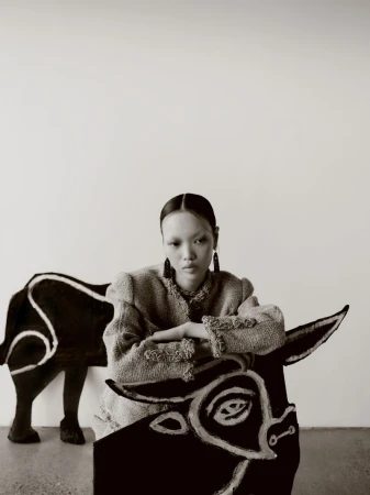 Model Weiyi Fang wearing a textured tweed jacket and leaning over a painted bull cutout against a plain studio backdrop.