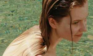 Woman with wet hair submerged in clear shallow water with a visible pebbly riverbed in natural sunlight.