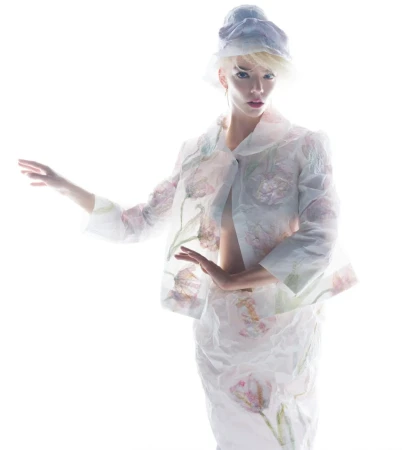 Anya Taylor-Joy posing in a sheer white floral printed jacket, matching skirt, and headpiece against a pure white background.