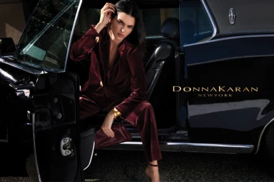 Kendall Jenner in a burgundy velvet pantsuit posing by a classic black car for Donna Karan Fall 2026
